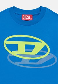 Modré tričko značky Diesel s žltým a svetlomodrým štýlizovaným logom "D" na prednej strane a červenou štítkou vo vnútri goliera.