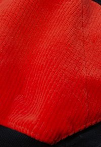 Gros plan sur un tissu en velours côtelé rouge avec des côtes verticales visibles et une couture, bordé par un bord en tissu noir.