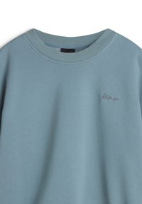Lichtblauw sweatshirt met een geribde ronde hals, zachte textuur en subtiele logo- borduursel aan de voorkant in een donkerdere blauw tint.