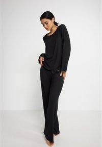 Ensemble de détente noir à côtes comprenant des manches longues et un pantalon à jambes larges. Les accents incluent une bordure ondulée aux poignets et à l'ourlet. Texture douce.