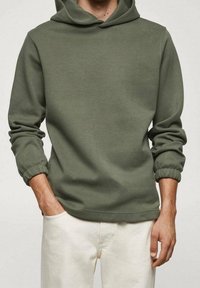 Sweat à capuche vert olive avec cordon de serrage, poignets côtelés et coupe décontractée. Fabriqué en tissu doux, il offre une texture lisse.