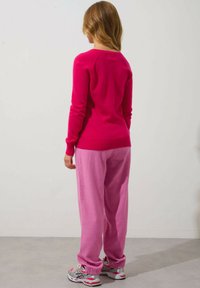 Fuchsia Pullover mit langen Ärmeln, kombiniert mit hellrosa Jogginghosen. Weiße und graue Sneaker mit pinken Akzenten. Rückansicht.