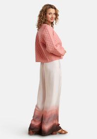 Roze gewatteerde cropped jack met een gestructureerd ruitpatroon. Vloeiende crèmekleurige broek met een gradient ombre ontwerp in roze en bruine tinten.