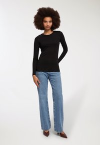 Czarna bluzka z długim rękawem zestawiona z jasnoniebieskimi spodniami typu wide-leg i brązowymi szpilkami, na jednolitym białym tle.