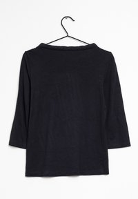 Camisa negra de manga larga con cuello redondo y aberturas laterales; hecha de un tejido suave; colgando de un gancho negro sobre un fondo blanco.