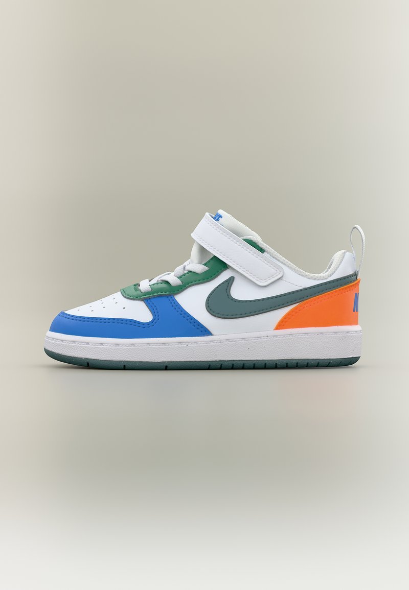 Baskets blanches avec des accents bleus, verts et orange, un swoosh Nike vert, des lacets blancs et une bride Velcro blanche sur un fond neutre.