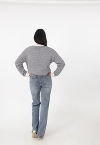 Szary, teksturowany sweter dzianinowy o szerokim kroju, zestawiony z wysokim stanem niebieskimi dżinsami. Białe mankiety podkreślają rękawy.