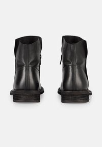 Bottes noires en cuir avec une finition légèrement texturée, dotées d'un talon bas superposé et d'une fermeture éclair latérale. Dessus à bout arrondi.