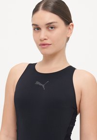 Black sleeveless athletic top made of stretchy material, featuring a reflective Puma logo on the chest and a fitted design.