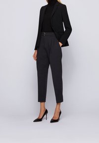 Musta räätälöity bleiseri ja istuva musta pooloneule, yhdistetty tummanharmaisiin korkeavyötäröisiin housuihin ja mustiin kärjellisiin korkokenkiin.