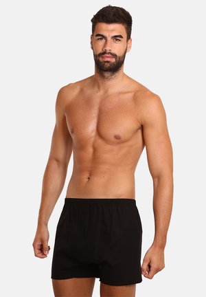 Boxers en coton noirs avec une taille élastique, conçus pour le confort, présentés sur un modèle avec le torse nu et les cheveux courts.