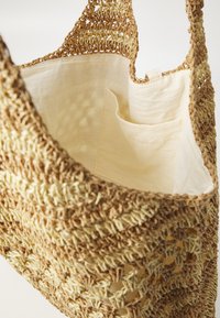 Woven tote bag in natural fibers with a textured, open-stitch design, featuring a beige fabric lining and an interior pocket.