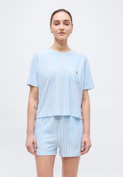 Woman wearing light blue and white vertical striped short-sleeve shirt and matching shorts on plain white background.