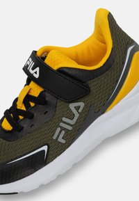 Zielone sportowe buty siatkowe z czarnymi i żółtymi akcentami, białą podeszwą, czarnym paskiem i logo marki w teksturowanym wzorze po boku.