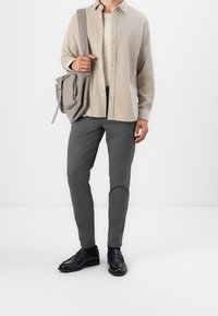 Hellbeiges Hemd mit Knöpfen, graue Slim-Fit-Hose, schwarze Lederschuhe und eine graue Umhängetasche mit Reißverschluss und Klappdetail.