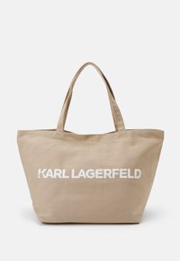 Beige canvas shoppingväska med två handtag, med djärv vit text "KARL LAGERFELD". Rymlig design, strukturerad form och hållbar textur.