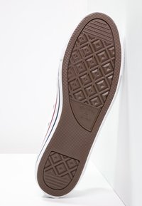 Hnědá gumová podrážka tenisky s diamantovým vzorem a horizontálními drážkami; bílý bok, červené a modré pruhy; vyražené logo s nápisem "Converse All Star."