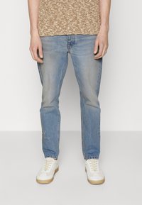 Ljusblå denimjeans med rak passform, som visar lätt blekning och slitningar. Kombinerade med vita och beige sneakers.