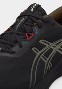 Κοντινό πλάνο μαύρου παπουτσιού για τρέξιμο ASICS Gel-Pulse 17 με μαύρα κορδόνια, γκρι λωρίδες λογότυπου, κόκκινες θηλιές για τα κορδόνια και καφέ εσωτερική επένδυση.