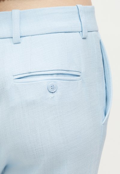 Φωτεινό γαλάζιο παντελόνι, ραμμένο στα μέτρα, με κουμπωτή πίσω τσέπη, ζώνη με θηλιές και πλαϊνή τσέπη, εμφανιζόμενο από την περιοχή του ισχίου.