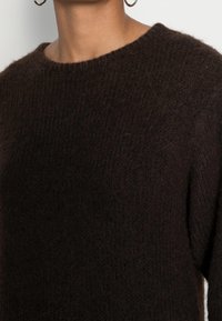 Brauner Strickpullover mit rundem Ausschnitt und langen Ärmeln, der eine weiche, strukturierte Oberfläche und einen leicht lockeren Schnitt aufweist.