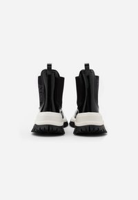 Bottines en cuir verni noir avec une semelle épaisse blanche. Dispose de panneaux latéraux élastiques et de languettes pour un enfilage facile. Semelle extérieure en caoutchouc texturé.