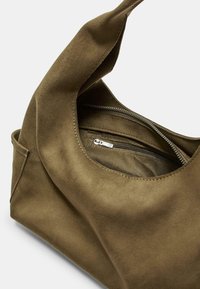 Sac en tissu vert olive au design décontracté, avec une poche zippée et une texture lisse. Comprend une poignée pour le transport.