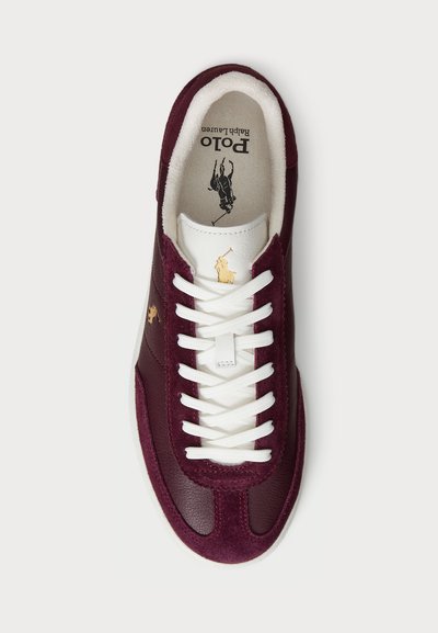 Sneaker bordeaux con lacci bianchi, in pelle liscia e suede, con logo dorato e colletto imbottito. Suola piatta in gomma.