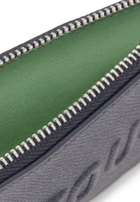 Pochette en tissu gris avec un intérieur vert, dotée d'une fermeture éclair argentée et d'un motif embossé sur l'extérieur. Texture lisse partout.