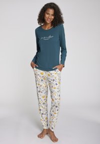 Långärmad teal topp med vit text; blommönstrade vita byxor med gula och lila blommor; lättviktigt material; avslappnad passform.
