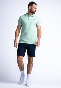 Ljusgrön polo med en liten logotyp, kombinerad med marinblå shorts. Bärs med vita sneakers och ankelsockor. Enkel, avslappnad outfit.