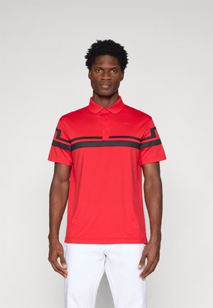 Raudona polo marškiniai su juodu dryžių raštu per krūtinę, trumpomis rankovėmis ir trimis mygtukais ant apykaklės. Sklandus, lengvas audinys.