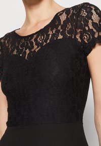 Top en dentelle noire à manches courtes, avec un motif floral et un col rond, associé à une partie inférieure noire ajustée.