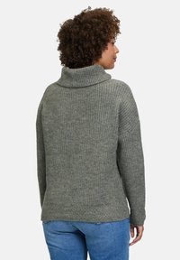 Grau gestrickter Pullover mit hohem Kragen, ausgestattet mit strukturierter Rippoptik und überschnittenen Schultern, kombiniert mit blauen Jeans.