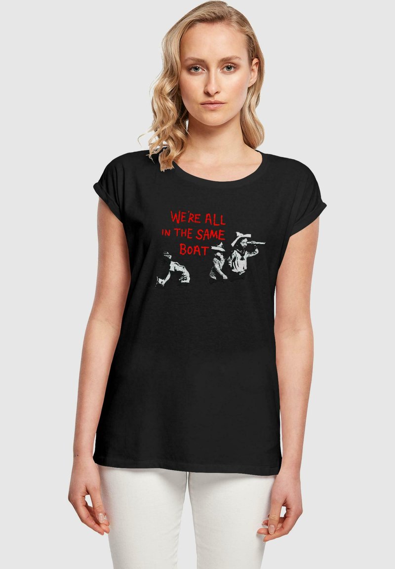 Black short-sleeve t-shirt featuring white and red graphic text: "WE'RE ALL IN THE SAME BOAT," with illustrated figures in action.