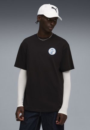 Sort bomulds T-shirt med korte ærmer, prydet med et blåt og hvidt cirkulært logo. Kombineret med en hvid kasket med et sort logo.