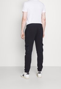 Černé cargo kalhoty vyrobené z bavlněné směsi, s dvěma bočními kapsami a elastickým pasem. Spárovány s bílými teniskami a přiléhavým bílým tričkem.