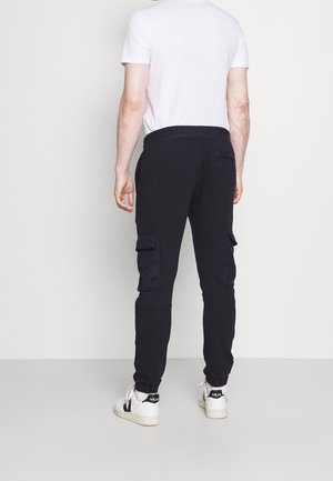 Zwarte cargojoggingbroeken van een katoenmix, met twee zijzakken en een elastische tailleband. Gecombineerd met witte sneakers en een aansluitend wit shirt.