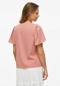 Blusa rosa con maniche corte e a sbuffo, caratterizzata da una trama liscia e un design semplice. Il retro è semplice, senza embellishments visibili.