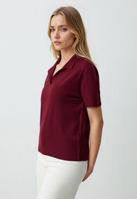 Burgundowa koszulka polo z krótkim rękawem z miękkiej dzianiny, z kołnierzykiem w kształcie litery V i prążkowanym dołem, w połączeniu z białymi spodniami.