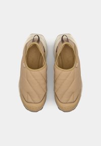Tenisi bej slip-on cu o textură matlasată, vârfuri rotunjite și o talpă din cauciuc alb. Prezintă un logo subtil pe lateral și un căptușel moale.