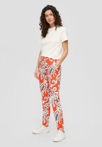 T-shirt blanche à manches courtes associée à un pantalon rouge à motifs avec des designs en paisley bleu et blanc, agrémentée de baskets blanches.