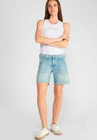 Shorts en denim bleu clair avec une coupe décontractée, des poches avant et une ceinture. Associés à un débardeur blanc ajusté et des baskets blanches.