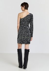 Miniabito nero con paillettes, una spalla, tessuto testurizzato, design aderente, abbinato a stivali neri fino al ginocchio con fibbie laterali.