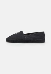 Sort espadrille med en tekstureret overdel, der har et diskret mønster, afsluttet med en vævet jute mellemsål og en metal logo accent.