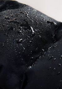 Des gouttelettes d'eau perlent et roulent sur une surface lisse en tissu noir résistant à l'eau.