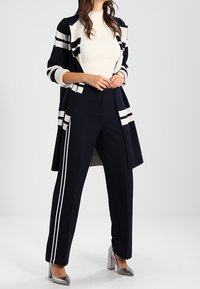 Marinblå cardigan med randiga accenter, vit ribbad tröja och marinblå byxor med sidostripes. Silverfärgade klackskor i blockmodell fulländar looken.