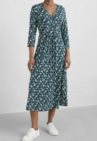 Laivastonsininen kukkakuvioinen mekko, jossa V-pääntie, puolipitkät hihat ja vyötäröltä poimittu leikkaus, tehty kevyestä kankaasta. Yhdistetty valkoisiin tennareihin.