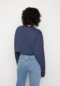Sudadera recortada de color marino con mangas largas, cuello redondo y dobladillo acanalado, combinada con vaqueros de talle alto en azul claro con bolsillos traseros.