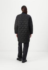 Zwarte gewatteerde jas met hartpatroon stitching, lange mouwen en een relaxte pasvorm, gecombineerd met donkere jeans en zwarte plateauboots.